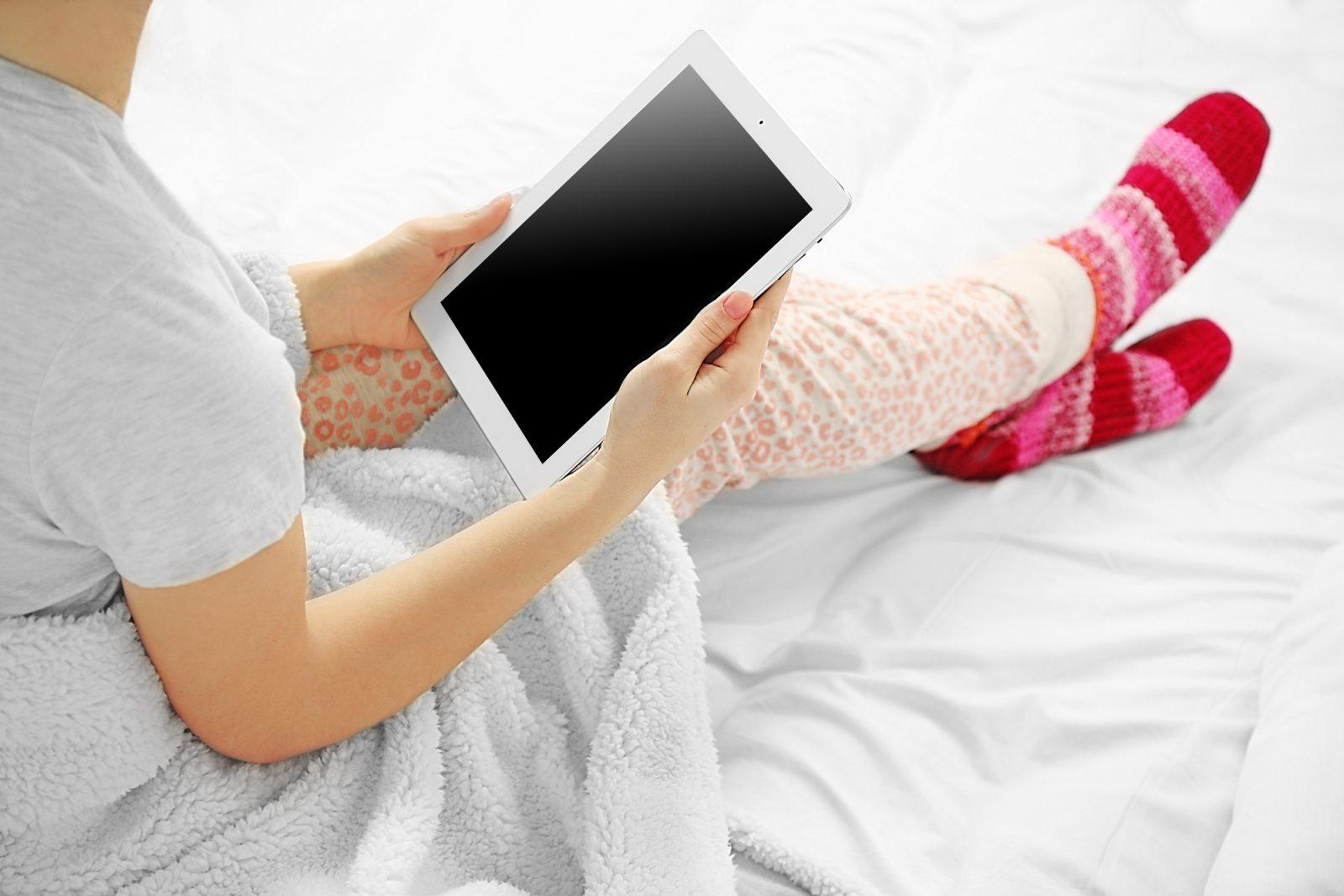 Woman in pajamas using a tablet on her bed